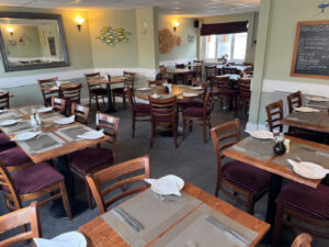 Picture of the inside layout of Janes Upstairs, wooden chairs, green walls with fish decor. Tablets set with placemats, cutlery and plates with salt and vinegar