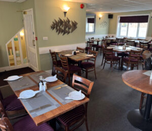 Picture of the inside layout of Janes Upstairs, wooden chairs, green walls with fish decor. Tablets set with placemats, cutlery and plates with salt and vinegar