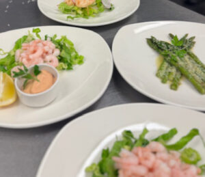 Lots of plates of food including prawns with seafood sauce, a plat of asparagus with parmesan topping.